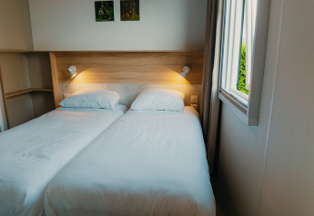 Zwei Einzelbetten mit weißer Bettwäsche in einem Zimmer der Family Lodge im Ferienpark De Boshoek, Niederlande.