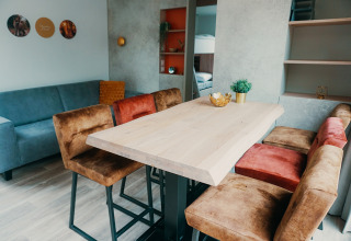 Salon du Family Lodge au Holiday Park De Boshoek, avec table en bois, chaises douillettes et canapé bleu.