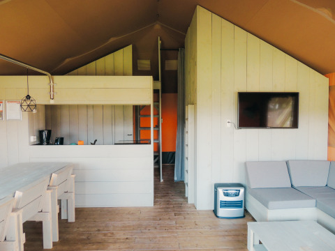Interior de una cabaña safari con cocina, comedor, sofá y TV en Holiday park De Boshoek, Países Bajos.