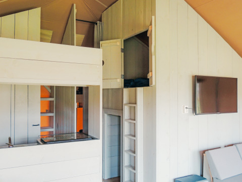 Interieur van de Safari cottage tent in Vakantiepark De Boshoek, met slaapgedeeltes en televisie aan de muur.
