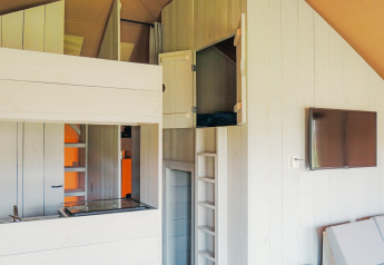 Innenaufnahme des Safari Cottage Zelts im Ferienpark De Boshoek mit Schlafbereich und Fernseher an der Wand.