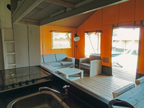 Innenaufnahme des Safari Cottage Zeltes mit Wohnbereich und Holzmöbeln im Holiday Park De Boshoek, Niederlande.