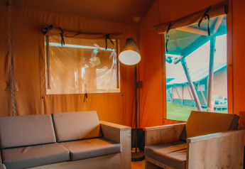 Interior de una cabaña safari con sofá y sillón en Holiday park De Boshoek, Países Bajos, vista desde una tienda.