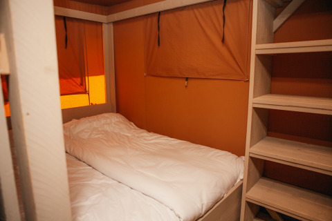 Inde i et Safari cottage-telt med en enkelt seng og træhylder i Holiday park De Boshoek, Holland.