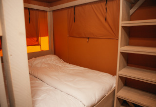 Inde i et Safari cottage-telt med en enkelt seng og træhylder i Holiday park De Boshoek, Holland.