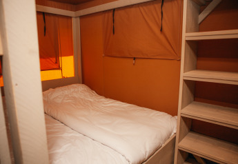 Binnenkant van een Safari cottage tent met een eenpersoonsbed en planken bij Holiday park De Boshoek, Nederland.