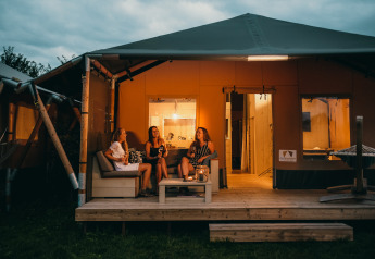 Tre donne si rilassano davanti a una tenda Safari House illuminata al Holiday park De Boshoek nei Paesi Bassi.