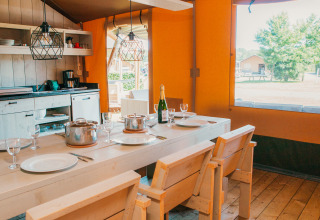 Vue intérieure de la Safari House au Holiday park De Boshoek aux Pays-Bas, avec table en bois et cuisine.