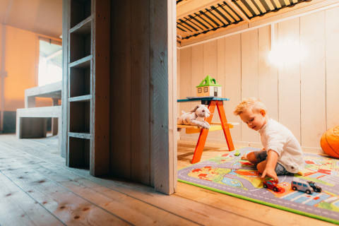 A child plays with toy cars on a colorful mat in the Safari House at Holiday park De Boshoek, Netherlands.