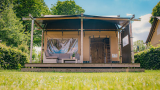 Luxury Safari lodge tent at Holiday park De Boshoek in the Netherlands, set against green hedges and trees.