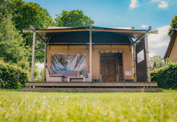 Luxe safaritent lodge op Vakantiepark De Boshoek in Nederland, gelegen tussen groene hagen en bomen.