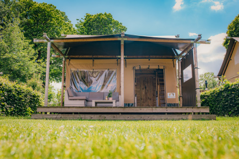 Luxury Safari lodge tent at Holiday park De Boshoek in the Netherlands, set against green hedges and trees.