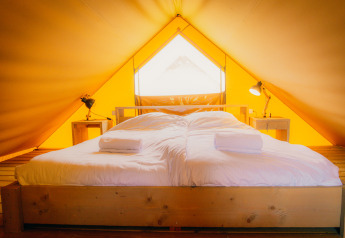 Binnenkant van een luxe Safari lodge tent op Holiday park De Boshoek met groot bed en nachtkastjes.