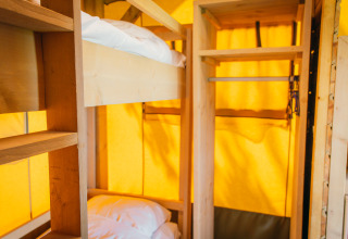 Interieur van een luxe safaritent met stapelbedden en opbergruimte bij vakantiepark De Boshoek in Nederland.