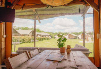 Uitzicht vanuit een luxe safarilodge op Holiday park De Boshoek in Nederland, met tafel en tenten buiten.