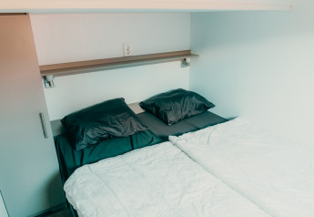 Letto matrimoniale moderno con cuscini scuri e lenzuola bianche a Veluwe lounge + sauna, De Boshoek.