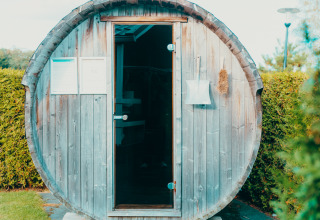 Een tonvormige sauna bij Veluwe lounge + sauna op vakantiepark De Boshoek, omgeven door groen.