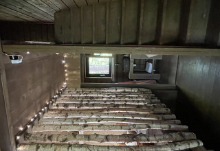 Interno di una cabina in legno accogliente con letti di tronchi di betulla e luci a Comfort Sweet Wellness.