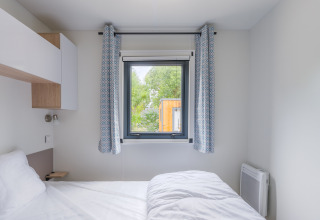 Lichte slaapkamer in Prestige Cottage, Camping Seasonova Haliotis, Frankrijk, met raam en wit beddengoed.