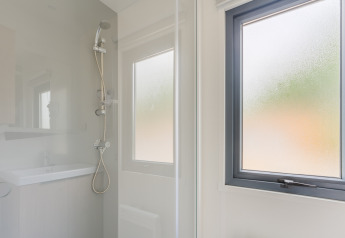 Moderne Dusche mit abgetöntem Fenster im Prestige Cottage auf Camping Seasonova Haliotis, Frankreich.