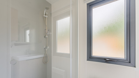 Douche moderne avec fenêtre givrée dans le Prestige Cottage au Camping Seasonova Haliotis, en France.