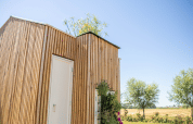 Houten lodge met groene beplanting en witte deur bij Het Eilandhuis, 7Huizen aan Zee, België, op een zonnige dag.