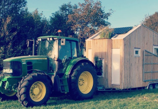 Grøn traktor trækker et lille træhus med solpaneler på græsset ved Het Eilandhuis, 7Huizen aan Zee.