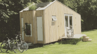 Kleines Holzhäuschen im Het Eilandhuis steht auf einer Wiese mit Fahrrädern, Terrasse und Bäumen.