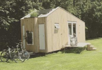 Una pequeña cabaña de madera en Het Eilandhuis en un campo con bicicletas, terraza y árboles al fondo.