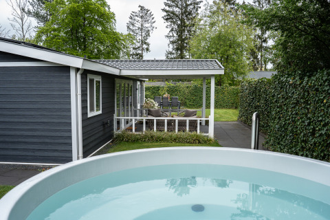 Vista exterior de Heuvelrug Cottage con porche, jacuzzi y seto verde en De Thijmse Berg, Países Bajos.