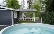 Vista exterior de Heuvelrug Cottage con porche, jacuzzi y seto verde en De Thijmse Berg, Países Bajos.