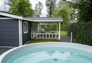 Udendørs udsigt over Heuvelrug Cottage med veranda, spabad og grøn hæk på De Thijmse Berg, Holland.