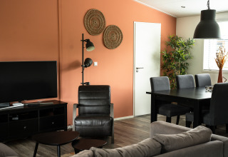 Sala de estar en Heuvelrug Cottage con muebles negros, pared naranja, televisor y plantas de interior.