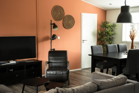 Stue i Heuvelrug Cottage med sort møblement, orange væg, tv, spisebord og grønne planter.