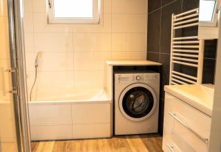 Modernes Bad mit Waschmaschine, Badewanne und Handtuchheizkörper im Heuvelrug Cottage, De Thijmse Berg, Niederlande.