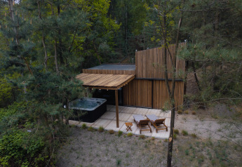 Moderna cabina in legno nella foresta con patio, sdraio e vasca idromassaggio presso Comfort Sweet Wellness in Limburgo, Belgio.