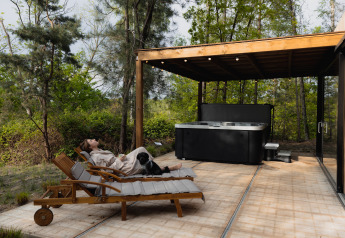 Donna rilassata con il suo cane su una sdraio vicino alla vasca idromassaggio a Comfort Sweet Wellness, Cosy Cabins, Limburgo, Belgio.