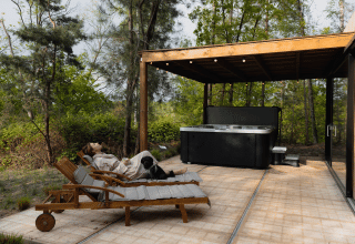 Mujer relajándose con su perro en una tumbona junto a un jacuzzi en Comfort Sweet Wellness, Cosy Cabins, Limburg, Bélgica.