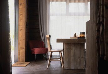 Acogedor interior de cabaña con muebles de madera, silla roja y grandes ventanas en Limburg, Bélgica.