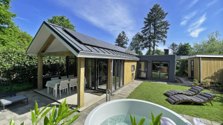 Vista esterna del Wellness Cottage a De Thijmse Berg, Paesi Bassi, con idromassaggio, sdraio e giardino.