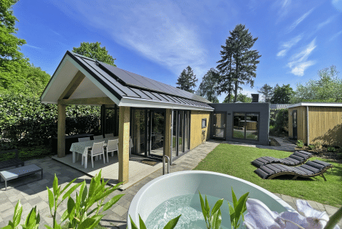 Vue extérieure du Wellness Cottage à De Thijmse Berg, Pays-Bas, avec jacuzzi, chaises longues et jardin.
