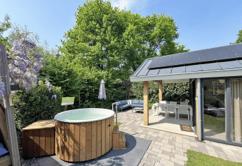 Wellness Cottage ved De Thijmse Berg i Holland, med udendørs badekar, terrasse og have under blå himmel.