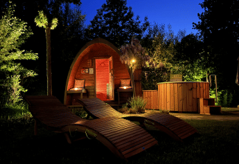 Knus wellnesshuisje met hottub en houten ligstoelen ’s avonds bij De Thijmse Berg in Nederland.