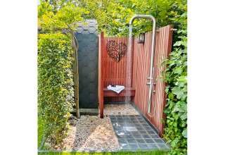 Ducha exterior en Wellness Cottage, De Thijmse Berg, Países Bajos, rodeada de madera y vegetación.
