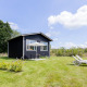 Sort tiny house med terrasse og liggestole på en grøn græsplæne under blå himmel med skyer.