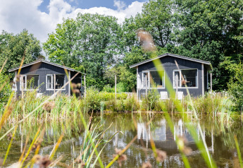 Dos cabañas Tiny House XL junto a un estanque en The Kremmer, Países Bajos, rodeadas de naturaleza verde.
