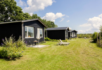 Reihe schwarzer Tiny Houses mit Terrassen und Sonnenliegen auf dem Rasen bei The Kremmer, Niederlande.