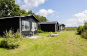 Reihe schwarzer Tiny Houses mit Terrassen und Sonnenliegen auf dem Rasen bei The Kremmer, Niederlande.