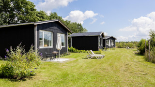 Reihe schwarzer Tiny Houses mit Terrassen und Sonnenliegen auf dem Rasen bei The Kremmer, Niederlande.