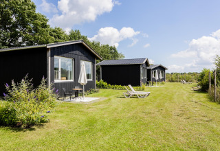 Reihe schwarzer Tiny Houses mit Terrassen und Sonnenliegen auf dem Rasen bei The Kremmer, Niederlande.